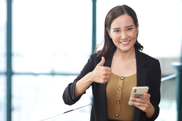 自信的年轻亚洲女商人在现代办公大楼和城市背景下使用智能手机进行商务会议，脸上带着快乐的微笑，研究和规划工作图片下载