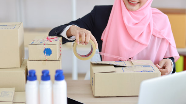 特写:活跃的亚洲穆斯林妇女双手穿着蓝色西装，坐在网上投递包裹。创业小公司中小企业自由职业女孩在电脑和手机工作的快乐的脸图片下载