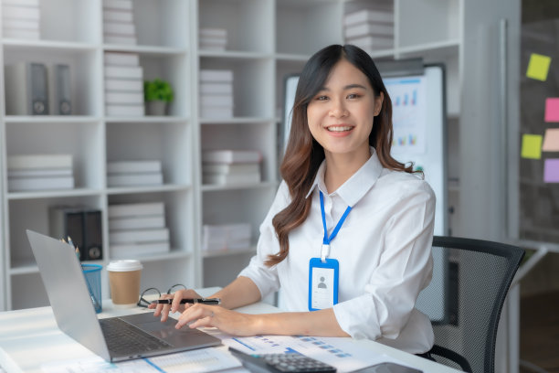 快乐微笑的亚洲女商人在办公室使用笔记本电脑。年轻漂亮的亚洲女性在社交网络上购物或聊天，在笔记本电脑项目上自由工作。图片下载