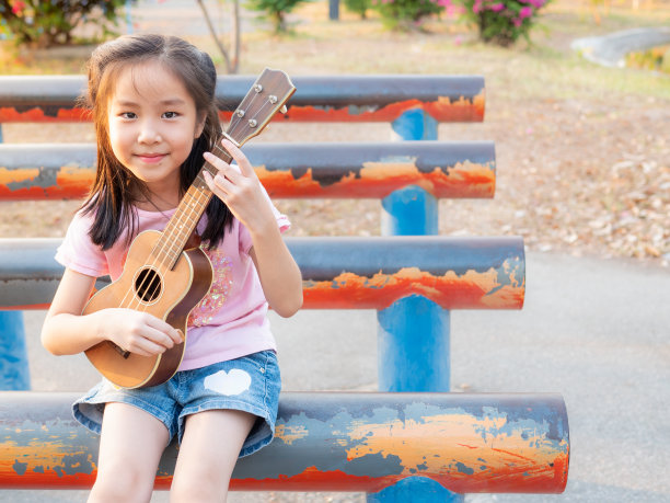 亚洲小女孩弹尤克里里，在花园的钢管上，练习演奏图片下载