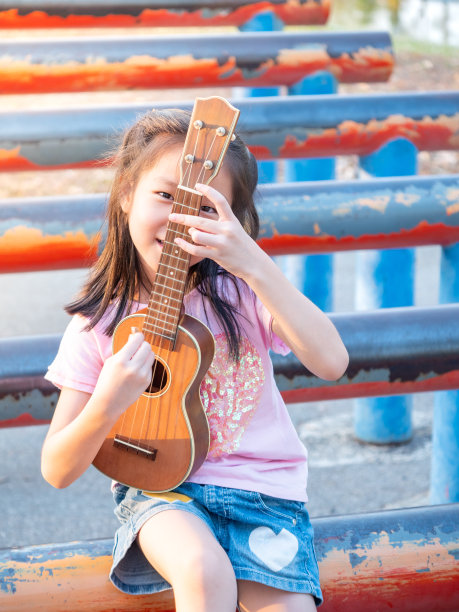 亚洲小女孩弹尤克里里，在花园的钢管上，练习演奏图片下载