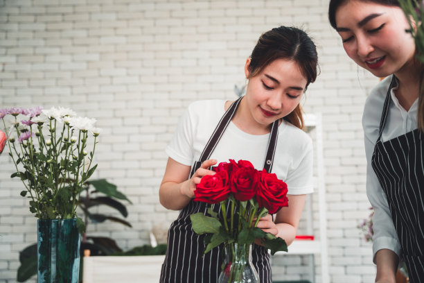 在花店里，两个年轻的花店老板笑容满面地装饰着一只玫瑰花瓶。图片下载