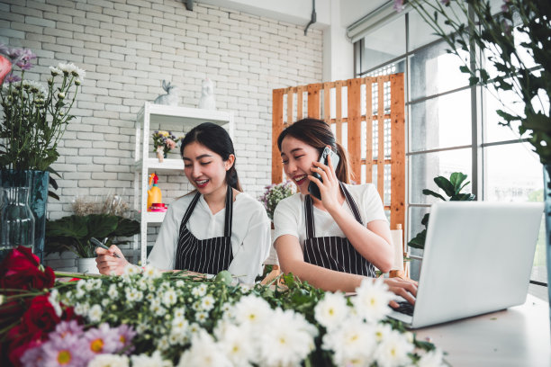 两名花店老板正在花店里插花，以吸引顾客的注意力，并通过智能手机接收顾客的订单。图片下载