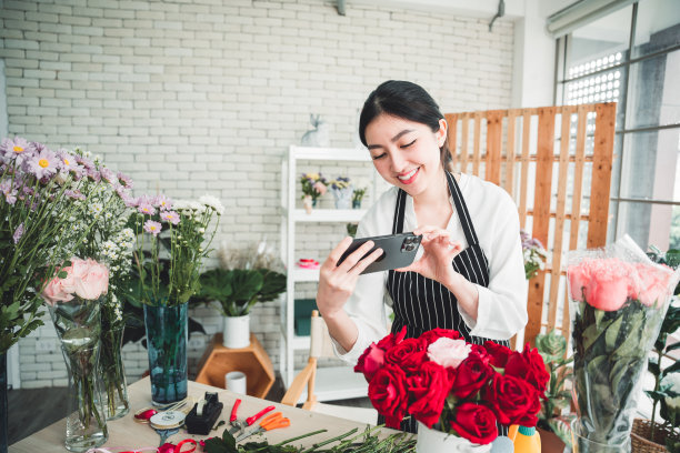 在花店里，年轻的花商正在为插在花瓶里的漂亮花朵拍照。图片下载