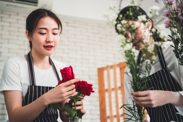 在一家花店，两个漂亮的女孩按照顾客的订单，精心地将鲜花切成玻璃花瓶，准备送到顾客手中。图片下载