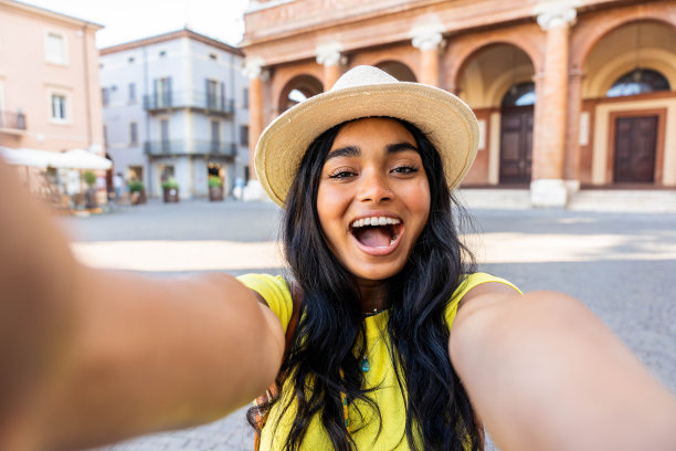 精彩的非洲女人对着镜头微笑——快乐的年轻亚洲女孩用智能手机自拍——博主网红访问西班牙图片下载