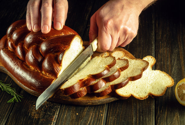 厨师的手用刀在厨房的砧板上切新鲜的面包或kolach作为午餐。健康食品和传统烘焙理念图片下载