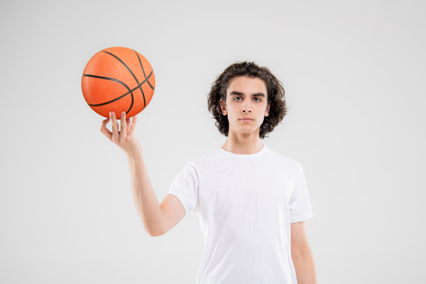 微笑的少年，篮球运动员在白色背景上拿着球摆姿势。图片下载