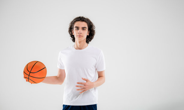 微笑的少年，篮球运动员在白色背景上拿着球摆姿势。图片下载