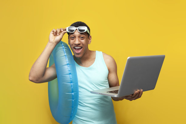 开朗的非洲裔美国人，戴着太阳镜，带着充气游泳圈，用黄色背景的笔记本电脑图片下载