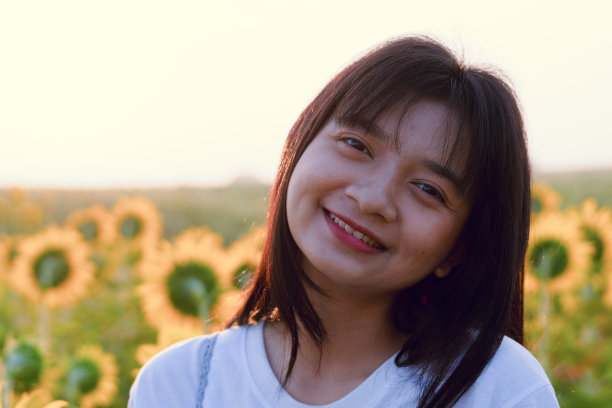 可爱的小女孩站在向日葵地里，清晨蓝天。图片下载