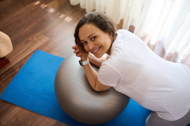 美丽的孕妇双膝站立，健身球运动，做产前伸展和呼吸练习图片下载