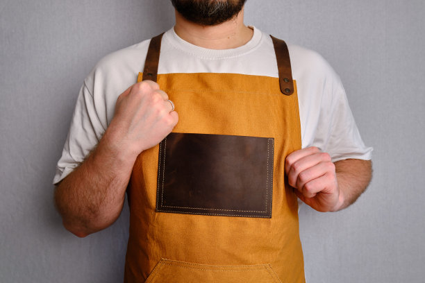 一个穿着厨房围裙的男人。厨师从事烹饪工作。穿着制服和防护服。食品服务方面的工作。专业烹饪。绿色面料围裙，休闲时尚服装。英俊的面包师摆姿势图片下载