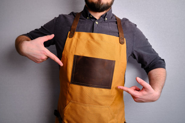 一个穿着厨房围裙的男人。厨师从事烹饪工作。穿着制服和防护服。食品服务方面的工作。专业烹饪。绿色面料围裙，休闲时尚服装。英俊的面包师摆姿势图片下载