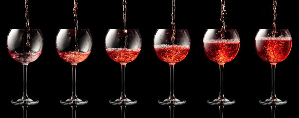 把粉红色的葡萄酒倒进黑色背景的杯子里。图片下载