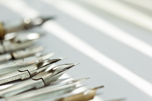 金属笔尖的墨水笔在太阳光线的白色背景。白色办公桌上的文具近距离俯视图。拼写课和书法练习。模板，布局，背景。宏图片下载