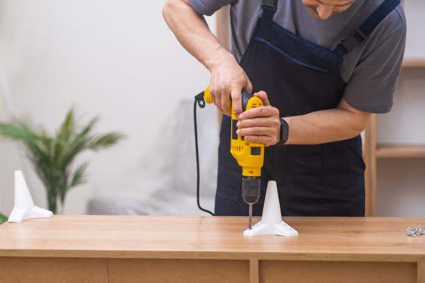 有经验的家具装配工，使用电动螺丝刀将腿固定在木架上图片下载