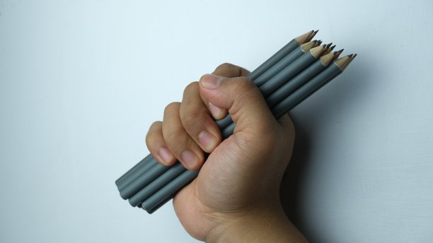 一只手握着白色背景上的一捆铅笔，概念性的图像。图片下载