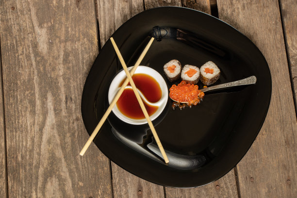 红鱼子酱放在寿司的勺子上，红鱼和酱油放在桌子上的黑色盘子里图片下载