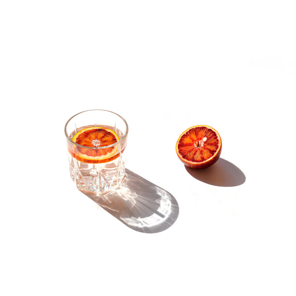 极简风格的创意组成，由半血红橙和一杯鸡尾酒在白色背景与阴影。夏日茶点和派对概念。图片下载