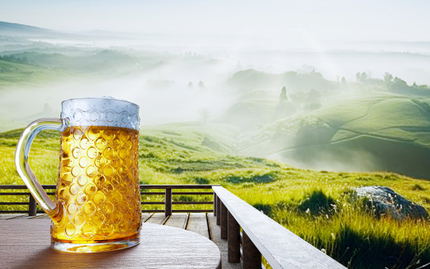 将生啤或精酿啤酒放在透明玻璃杯中，顶部有啤酒泡沫，放在一套木桌上。木质露台上的休息区与山的背景与上帝的光或阳光。三维渲染图片下载