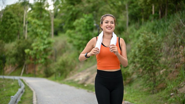 一个穿着运动服的快乐的亚洲女人喜欢独自在自然公园的街道上跑步图片下载
