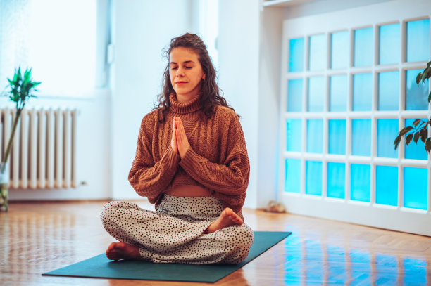 一个白人女孩坐在垫子上，摆出莲花的姿势，双手摆出祈祷的姿势。图片下载