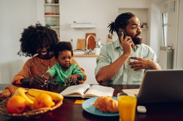一个跨种族忙碌的父亲忽视了他的家庭。一个男人正在接一个业务电话，而他的家人在他旁边玩。图片下载