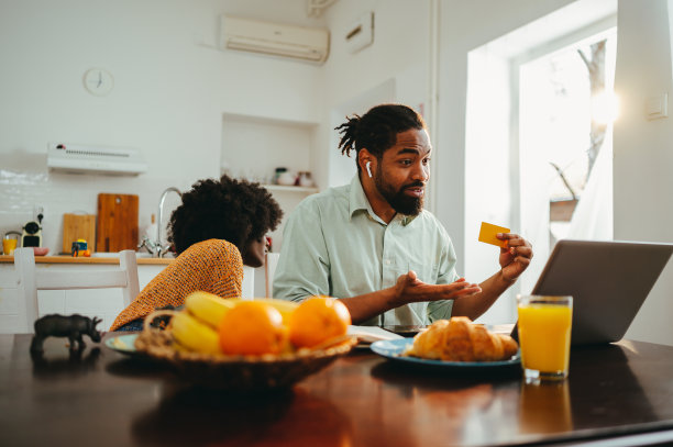 一个忙碌的跨种族丈夫正在笔记本电脑上进行电话会议，而他的妻子坐在家里的早餐桌上照顾她的儿子。图片下载