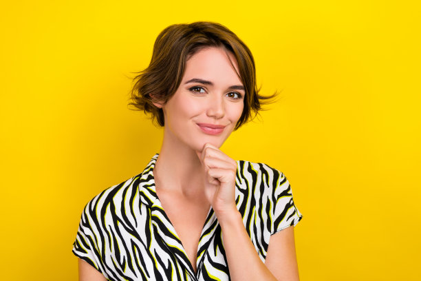照片中可爱的女士用手抚摸她的下巴，聪明的年轻工人穿着斑马衬衫，孤立的黄色背景图片下载