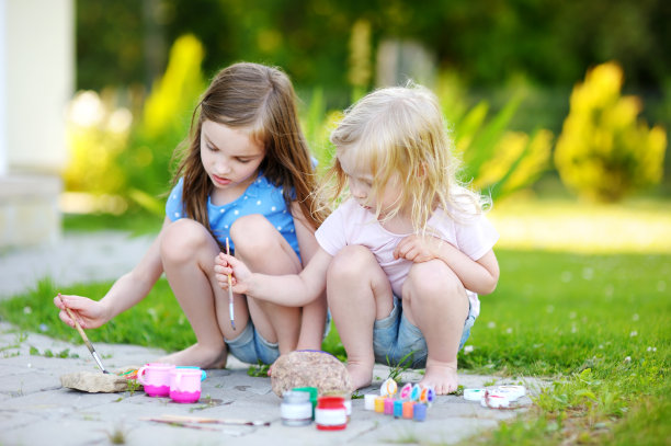 两个可爱的小姐妹一起在石头上画画图片下载