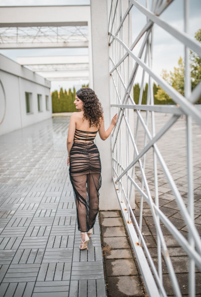 一个优雅的年轻毕业生的后视图，穿着优雅的黑色连衣裙图片下载