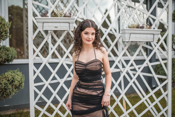 一个年轻的毕业女孩的肖像，穿着优雅的裙子，站在装饰着花盆的墙上图片下载