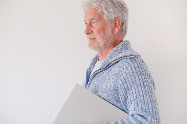 一位白发苍苍的老人腋下夹着一台笔记本电脑走着。享受科技和社交活动的老一代图片下载