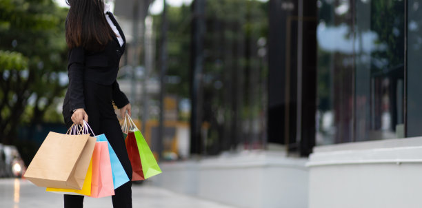 年轻美丽的亚洲女人拿着五颜六色的购物袋走在城市的街道上。快乐的女人拿着购物袋享受着购物。消费主义，生活方式的城市概念。图片下载