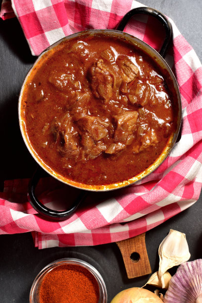 红色方格桌布上的旧搪瓷锅里的炖牛肉。从顶部看。垂直的照片。图片下载