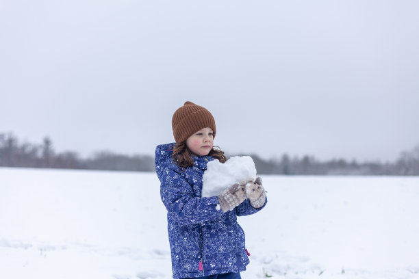一个穿着蓝色夹克，戴着针织帽的女孩手里拿着一个雪人。图片下载