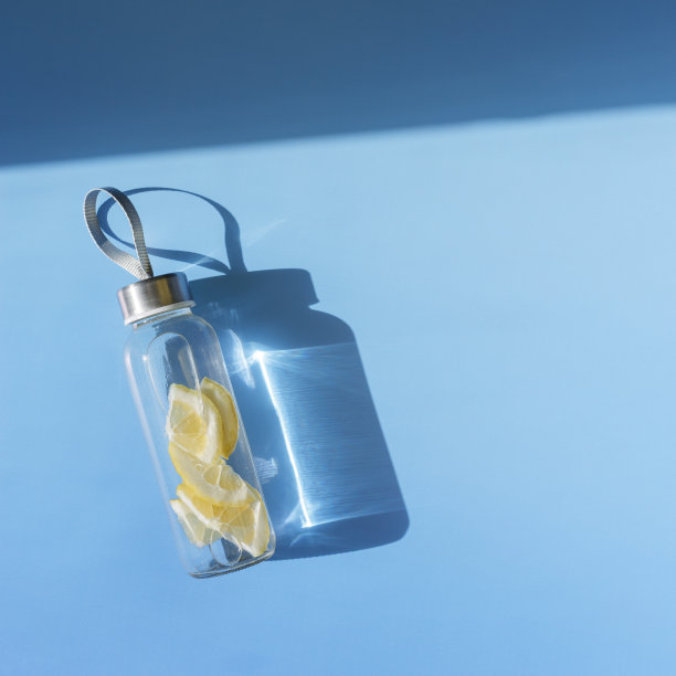 柠檬水喝排毒瓶，硬阴影在阳光下蓝色的背景。养生、饮食、饮食健康的理念。顶景玻璃可重复使用的水瓶，环保的生活方式，最小的照片图片下载