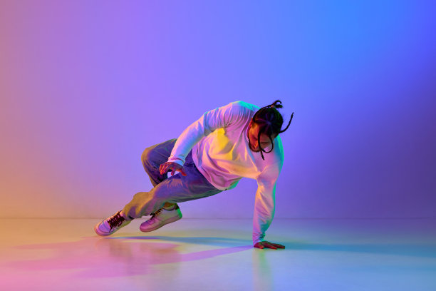 年轻人扎着辫子，穿着休闲服，在霓虹灯的渐变多色工作室背景下跳街舞、霹雳舞图片下载