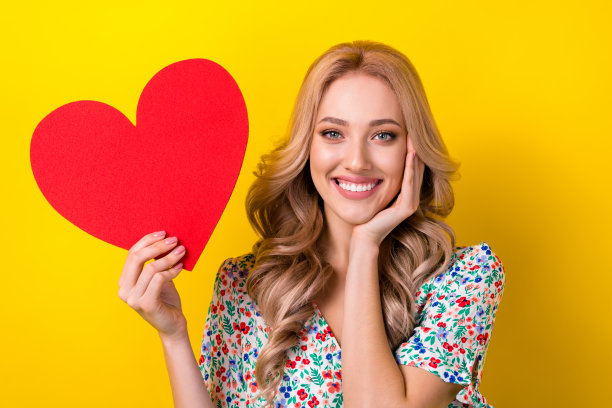 照片正面漂亮的女士穿着时髦的衣服，手握明信片手臂触摸脸享受浪漫的感觉孤立的黄色背景图片下载