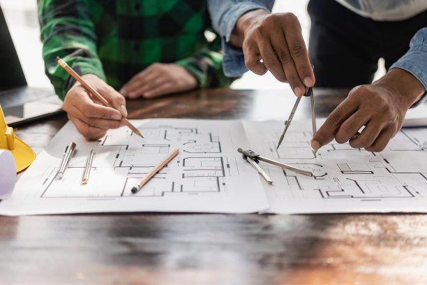 两个穿着黄色衣服的工程师在办公室的办公桌前与建筑工地的建筑项目讨论数据和笔记本电脑图片下载