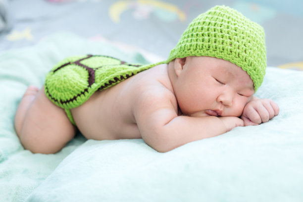 穿着海龟服装的孩子，一个一个月大的新生儿躺在一条毛巾上，在绿色的连衣裙下放松。图片下载