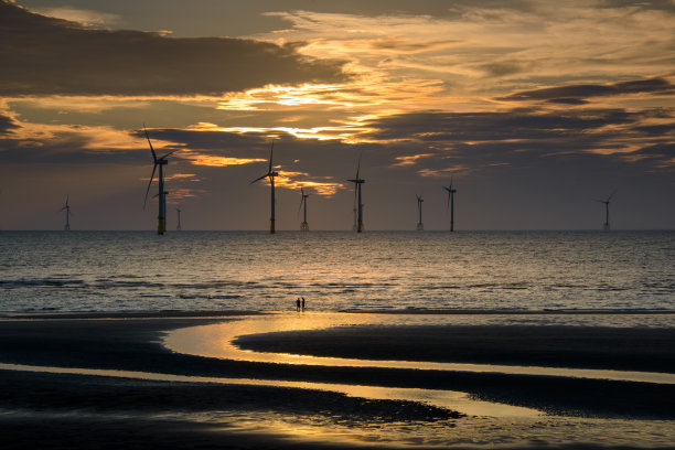 风力涡轮机的风扇在波光粼粼的海面上旋转。日落时的动态云。图片下载