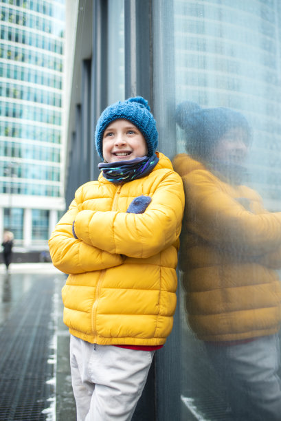 一个快乐的男孩在冬天穿着明亮的衣服在大都市的肖像图片下载