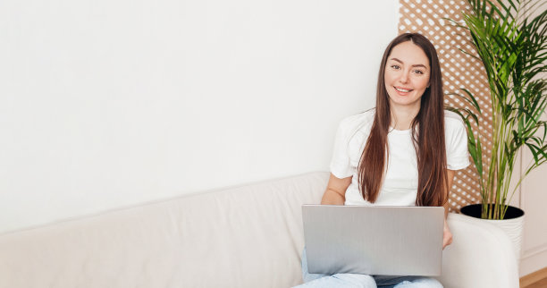 女孩坐在沙发上，带着笔记本电脑微笑着看着摄像头网页横幅图片下载