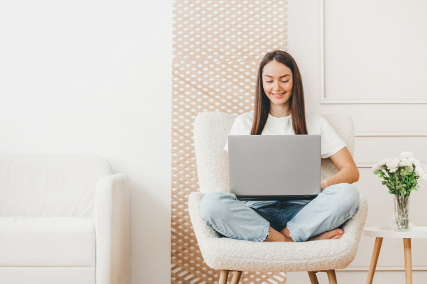 自由女孩坐在家里的椅子上，用笔记本电脑工作，背景是一堵白墙图片下载