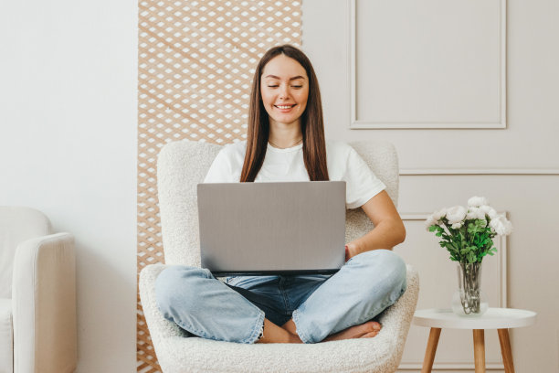 一个女孩倚着白墙在家用电脑工作的画像。自由职业者，在线培训，生活方式理念图片下载