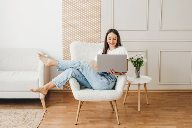 女学生在家用笔记本电脑。女人坐在椅子上微笑着看着电脑图片下载