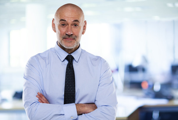 中年商人双臂交叉站在办公室里图片下载