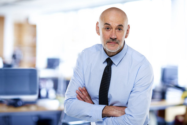 中年商人双臂交叉站在办公室里图片下载